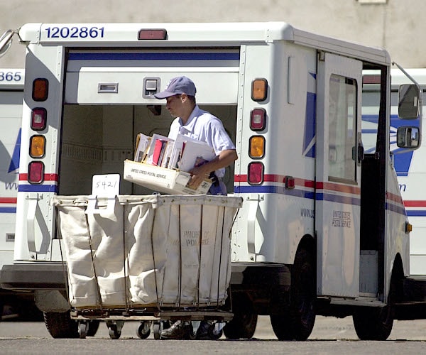 a postal service truck is unloaded by a mail man