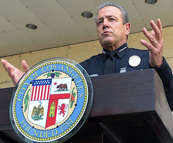 michal moore speaks to the media with the lapd shield on the podium