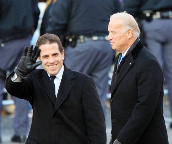 hunter biden waves to the crowd wearing a black coat while joe biden walks near him