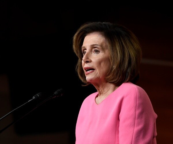 pelosi in a pink dress speaking into a mic