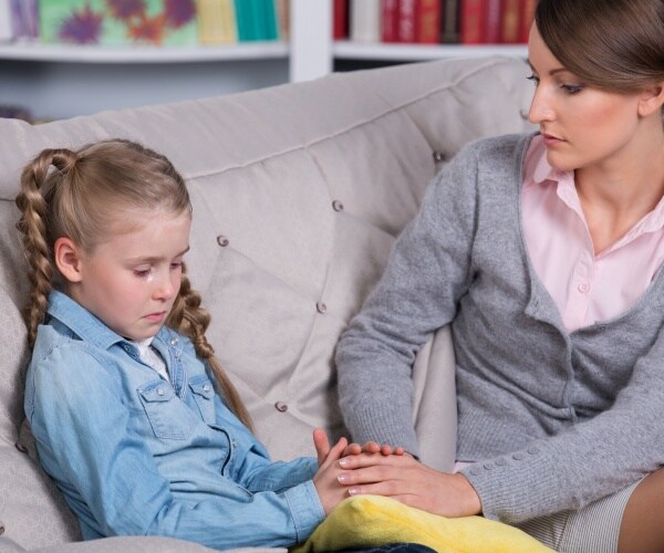 mother/counselor talking to girl on couch who is crying/anxious