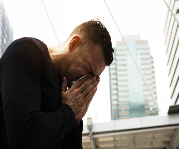 man sneezing/holding nose in a city