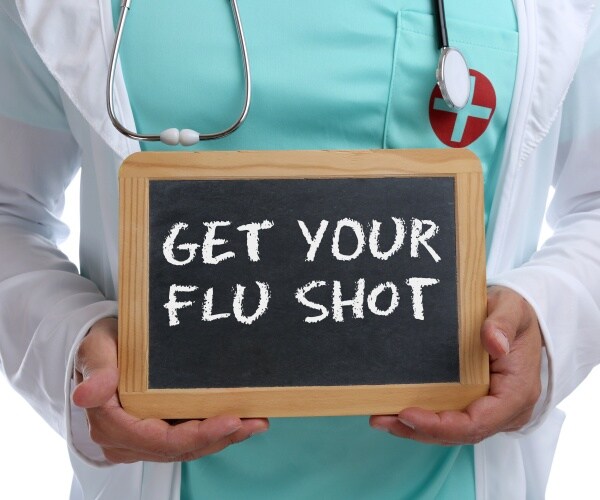 Doctor holding a chalkboard sign saying "Get Your Flu Shot"