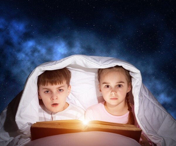 young boy and girl in bed at night with covers over their heads, using flashlights to read books