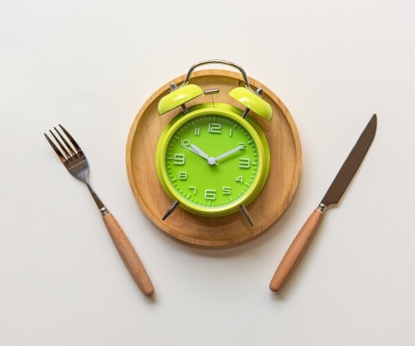 alarm clock on plate with knife and fork to illustrate intermittent fasting