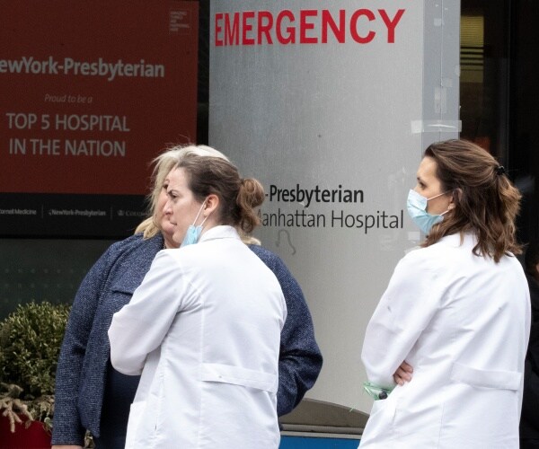 doctors in white coats and masks stand outside an emergency room at a hospital