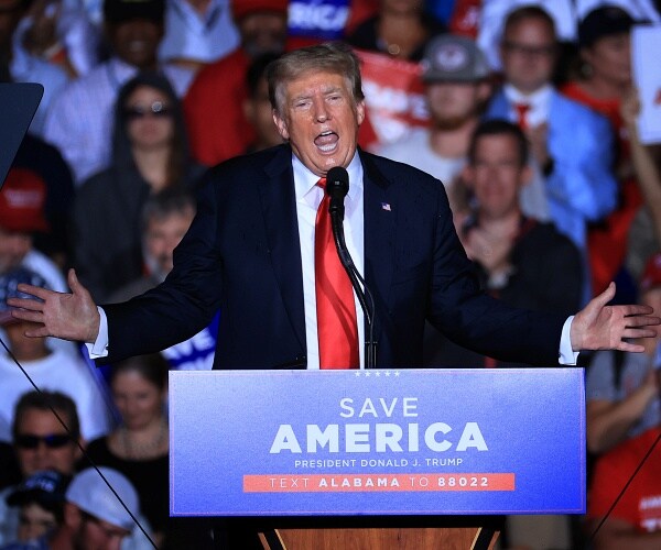 donald trump holds arms out while speaking onstage at rally