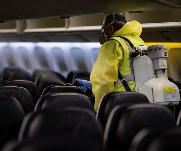 a person in a yellow hazmat suit disinfects the interior of an airplane