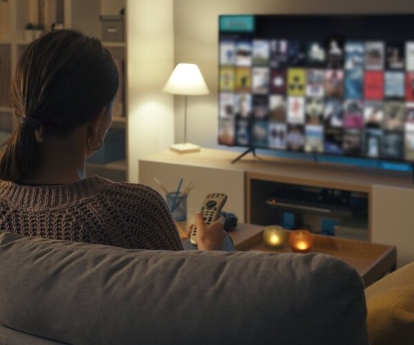 woman up late sitting on couch and using remote to look for something to watch on tv