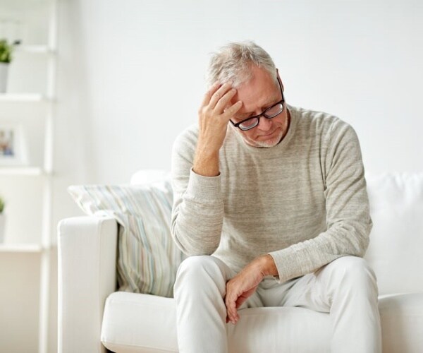 man sitting on couch looking sad, holding his head