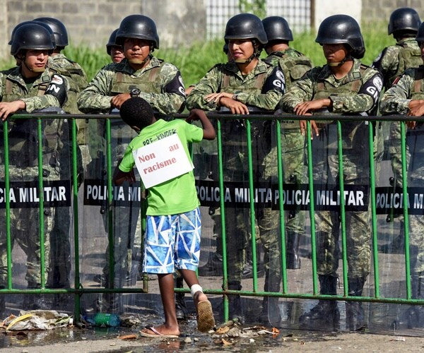 a boy in wears a sign protesting racism in mexico with police blocking