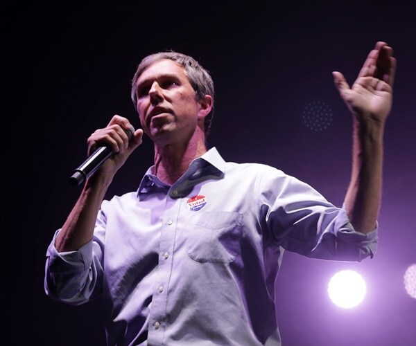 beto o'rourke speaks into a mic on stage in front of a bright light