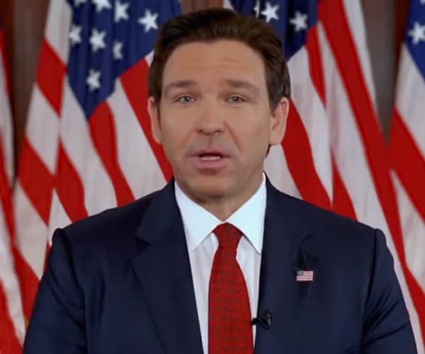 desantis speaking in front of a row of american flags