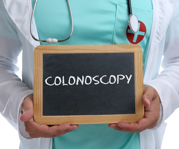 man with medical garb and stethoscope holds chalk board bearing the word colonoscopy