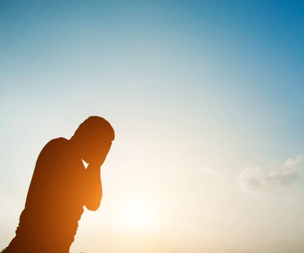 man outside in hot sun with head in hands, depressed