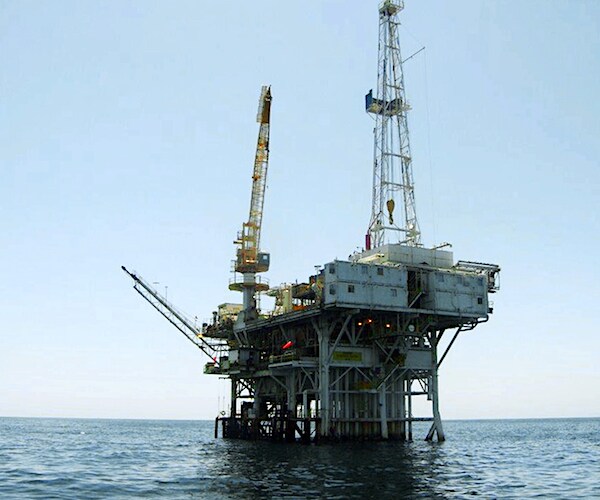 an offshore oil rig on the open ocean against a pale blue sky