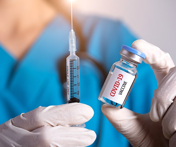 Female doctor with a stethoscope on shoulder holding syringe and COVID-19 vaccine