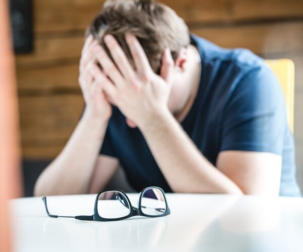 depressed man with head in hands on desk, glasses to the side