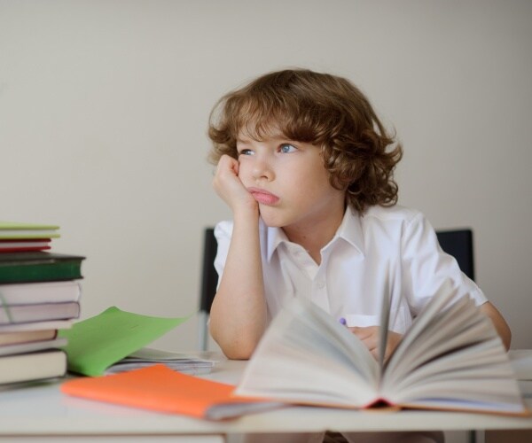 little boy with dyslexia looking off with a book open in front of him