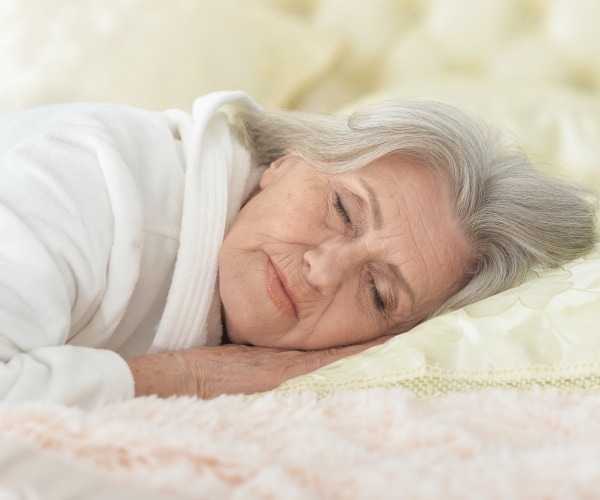 older woman sleeping soundly on pillow, cream-colored bedding