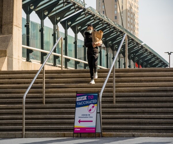 photo of a person walking downstairs outside with a mask and sign pointing to a covid vaccination site