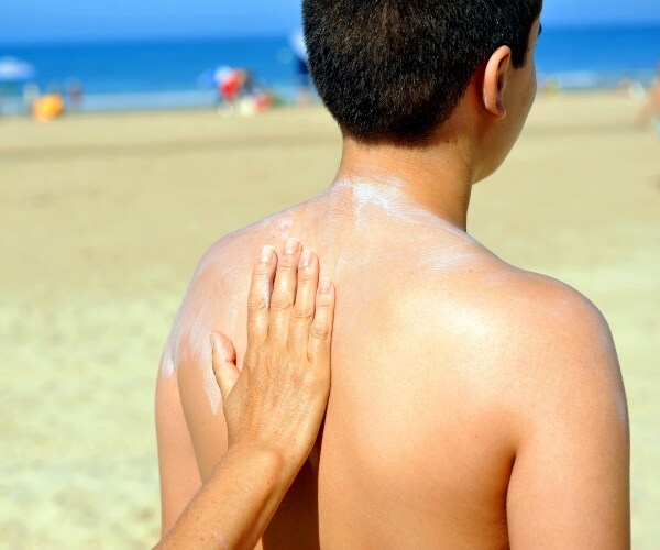 mother putting sunscreen on son's back at beach