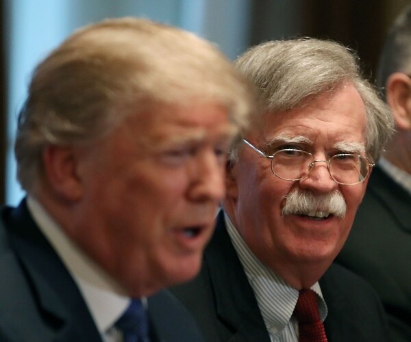 bolton looks at trump while he speaks wearing a dark red tie and striped shirt