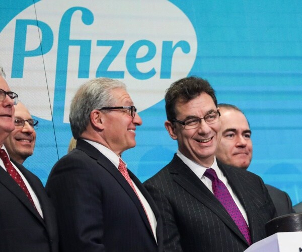 bourla in a purple tie and suit in front of a pfizer logo