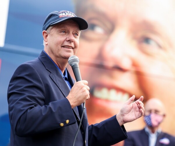 lindsey graham wears a baseball hat and speaks agains a big picture of himself