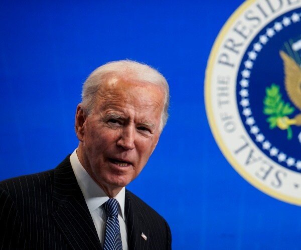 joe biden stands under the presidential seal against blue