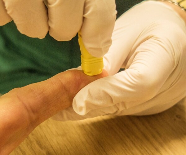 healthcare worker taking blood from finger prick