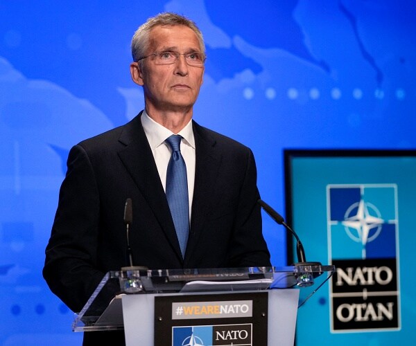 jens stoltenberg stands behind podium