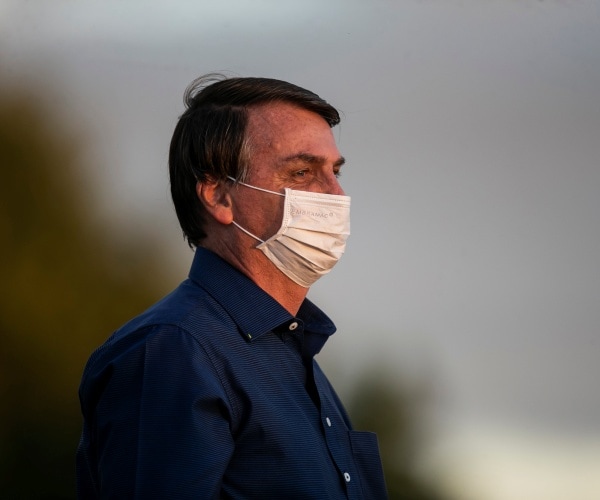 bolsonaro wearing a mask and navy blue dress shirt standing outside