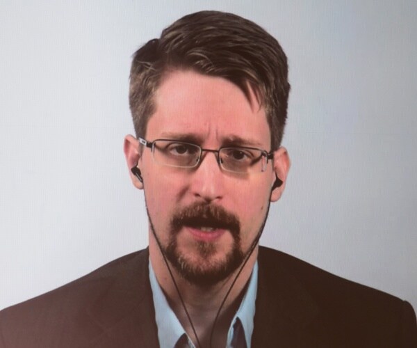 snowden in a suit and wearing earbuds speaking on a screen