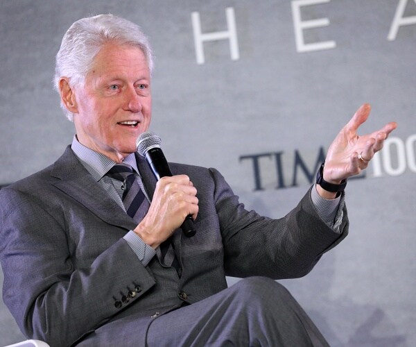 bill clinton sits onstage and speaks into handheld mic