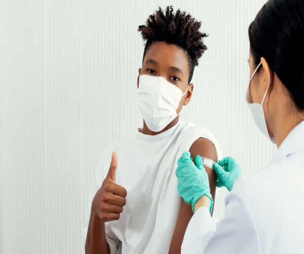 a teen boy giving thumbs up as he gets the COVID vaccine