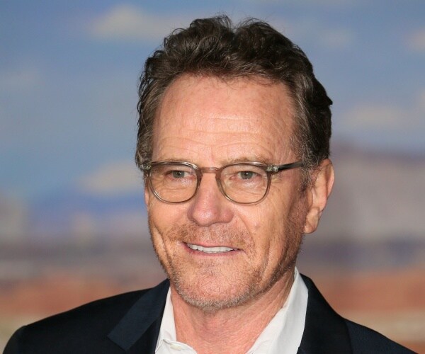 cranston in a black suit and white dress shirt wearing glasses