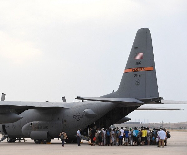 refugees stand on tarmac waiting to board jumbo plane