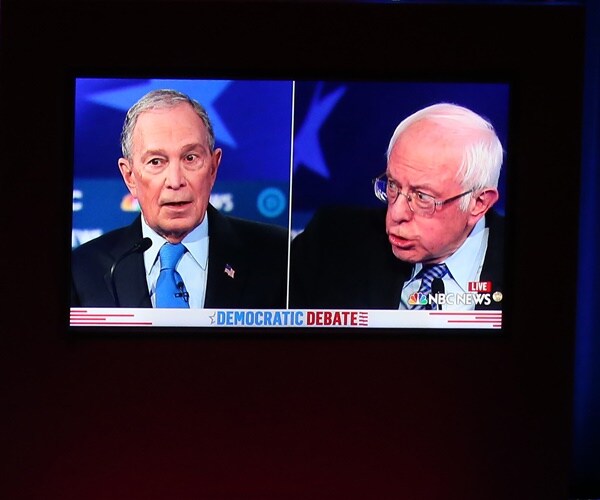 mike bloomberg and bernie sanders are on a monitor in a side by side.