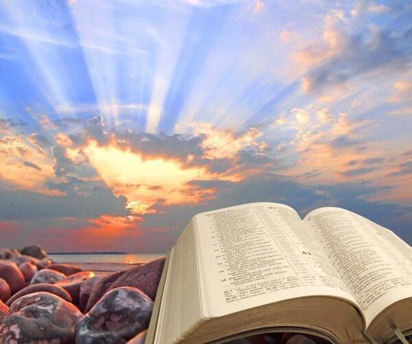 bible on rocks with sun over water