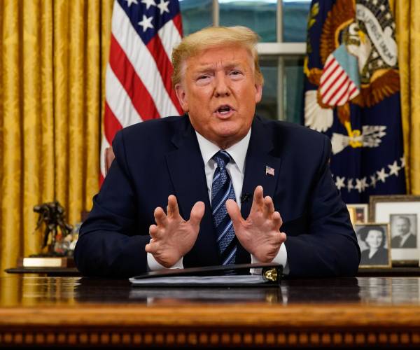 trump seated at desk speaking to camera