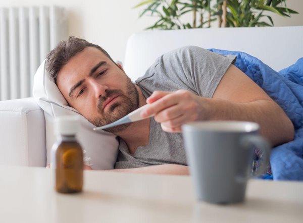 man on couch not feeling well taking his temperature. 