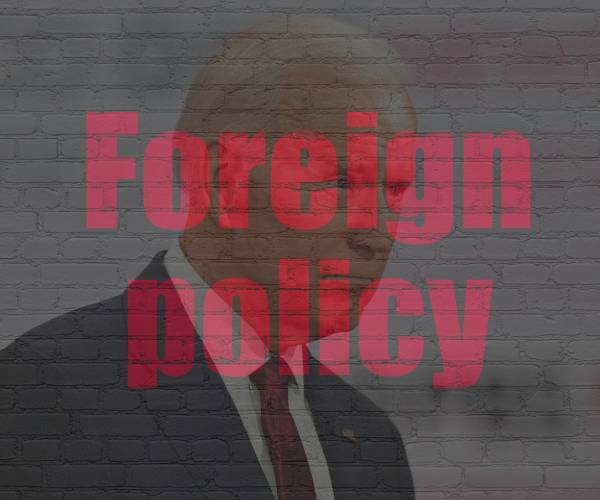 president joe biden behind brick wall with foreign policy written on it