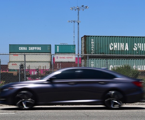  a car drives past shipping containers of goods from china