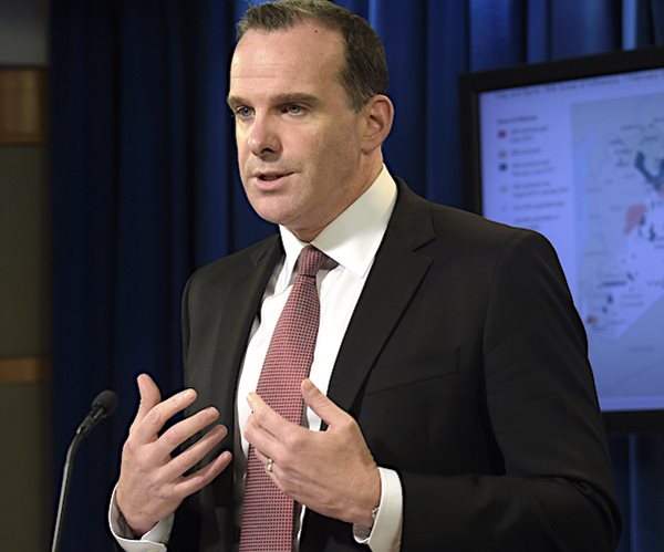 brett mcgurk motions to his chest with palms of both hands, speaking to a news conference in front of a syria map