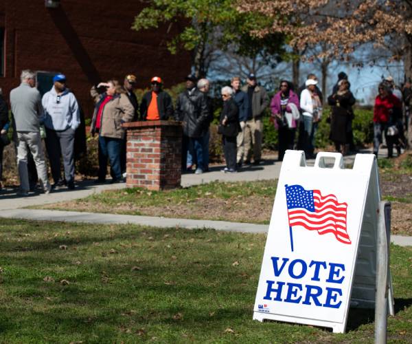 people in line with a sign reading vote here in the foreground