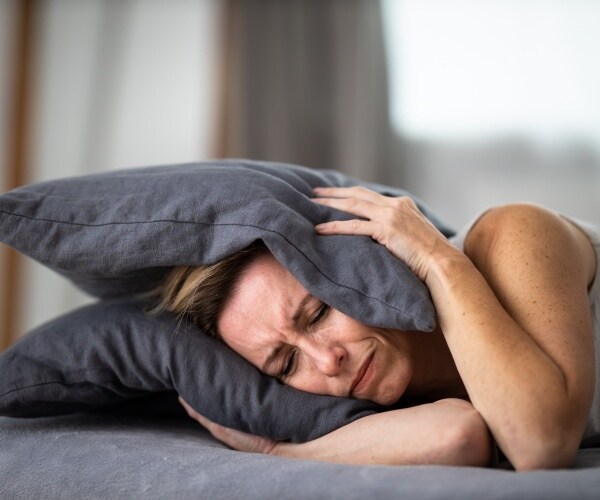 a woman in bed holding pillows on her ears 