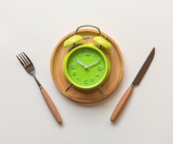 green alarm clock on plate with knife and fork on either side