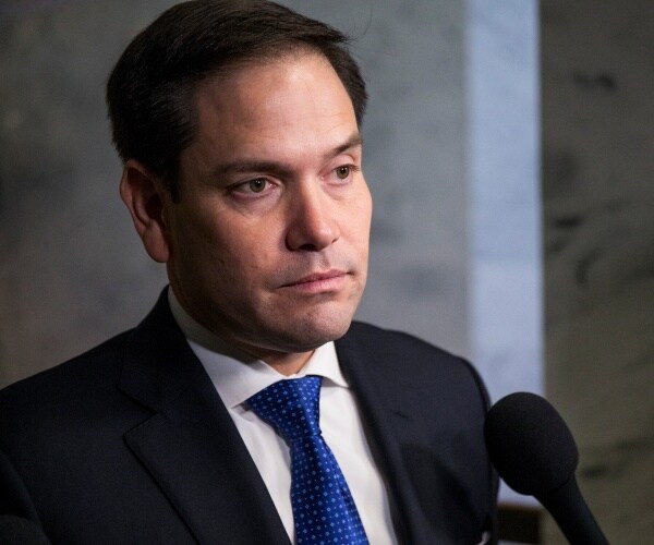 rubio in a black suit and blue tie speaking into a mic