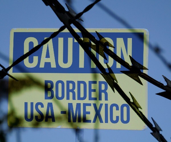 a sign reading caution border usa mexico behind razor wire